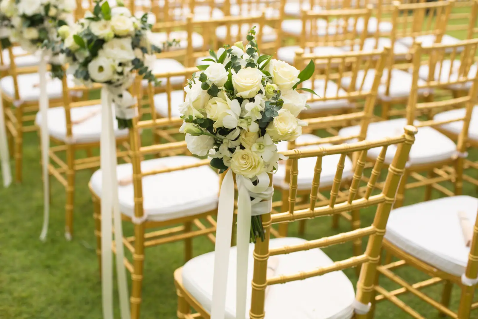 Gold Chiavari chairs with white floral arrangements set for an outdoor wedding ceremony